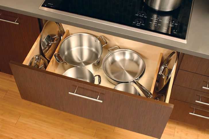 Хранить крышки или разделочные доски на кухне можно в разделителе для тарелок. Некоторые хозяйки к дну подвесного шкафчика крепят крючки, на которые за ручки вешают сковороды.